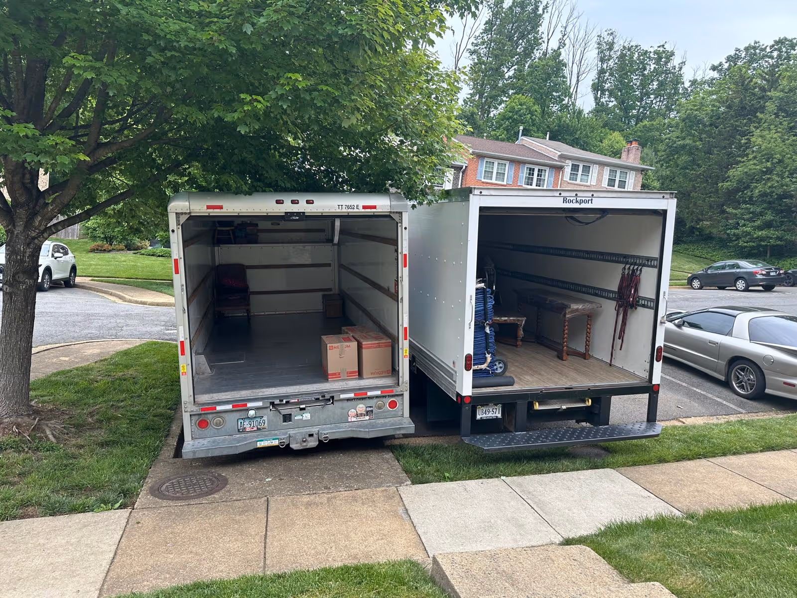 Two moving trucks parked side by side with their rear doors open, showing a few moving boxes and furniture inside.
