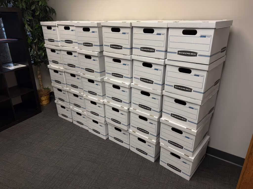 Stack of white Bankers Box file storage boxes arranged against a wall in an office setting.