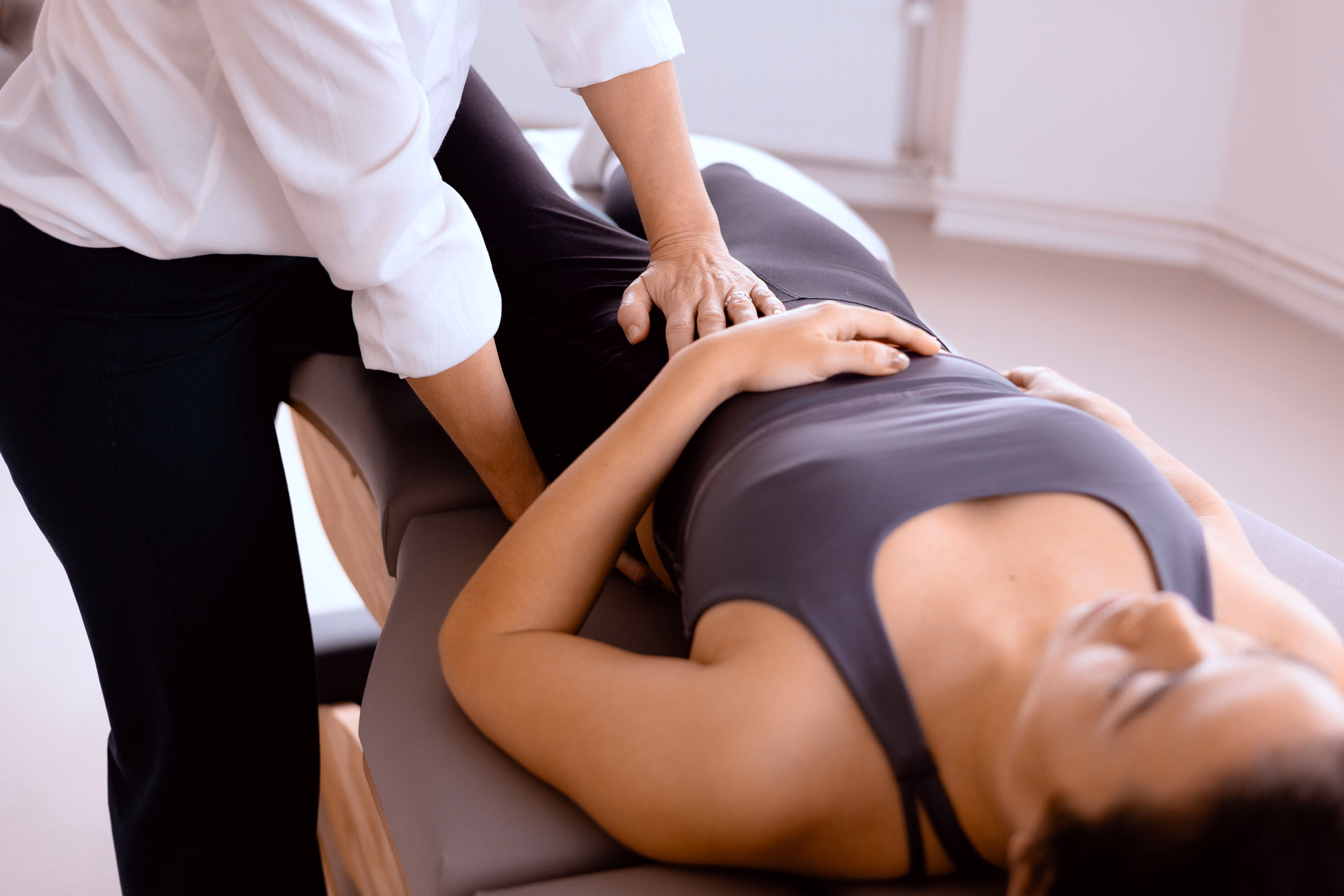 Osteopath behandelt das Becken einer liegenden Patientin