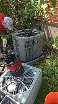 HVAC technician repairing air conditioning unit next to brick wall and plants