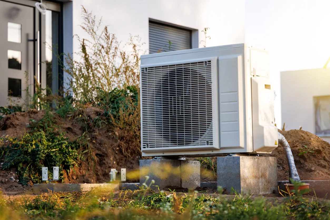 Heat pump installed outside modern building with overgrown vegetation