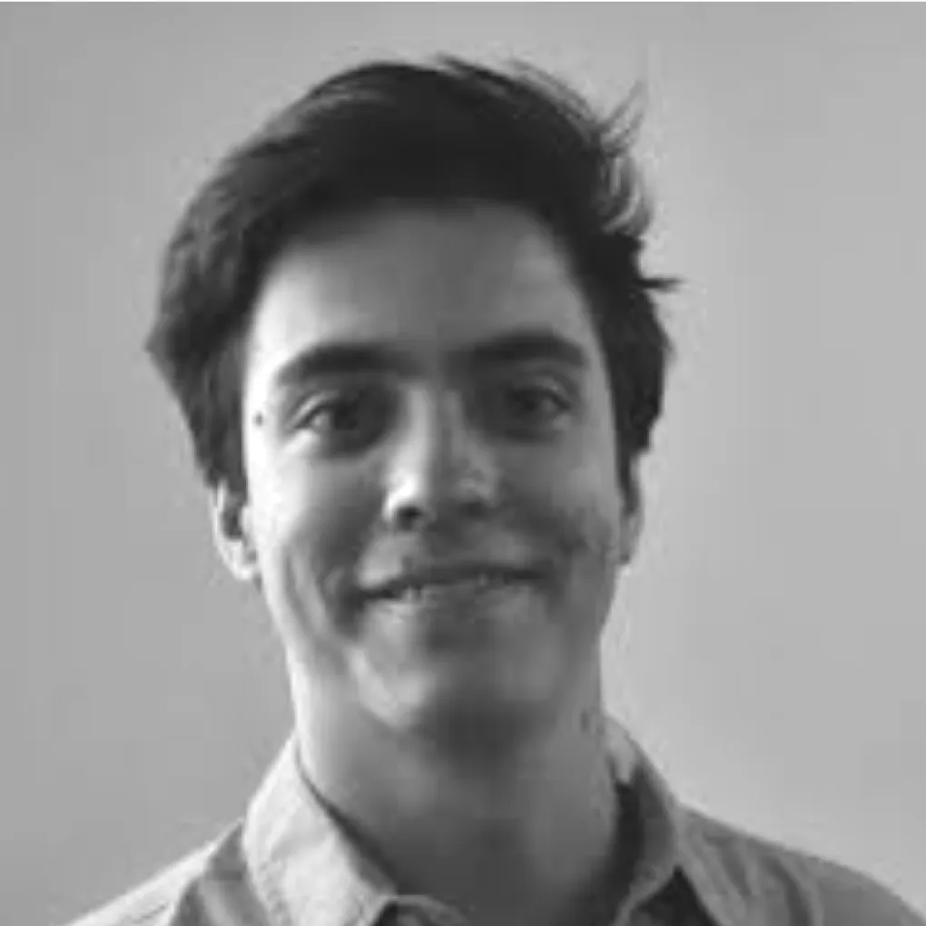 Young man with dark hair smiling slightly, wearing a collared shirt against a plain background.