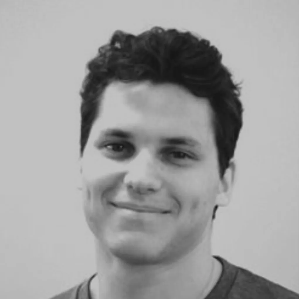 Smiling young man with curly dark hair in a grayscale close-up portrait.