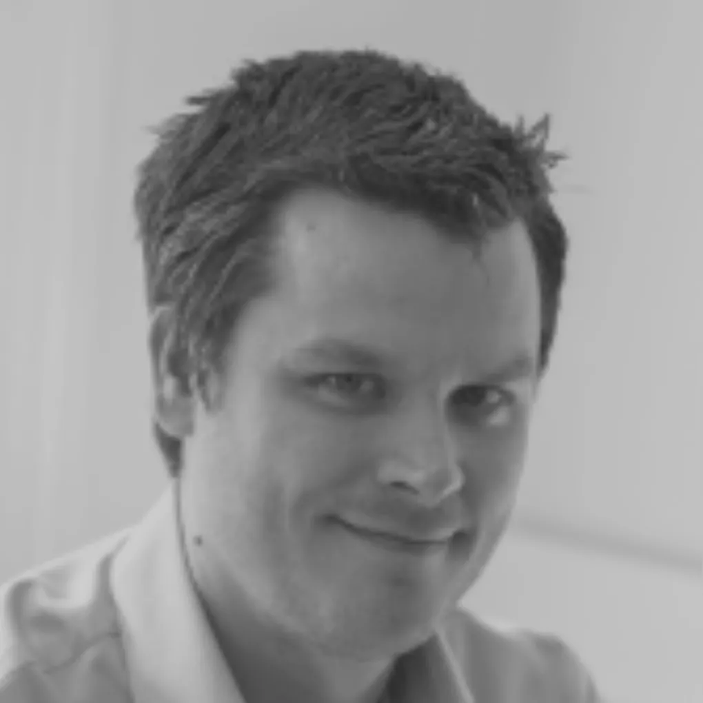 Close-up black and white portrait of a man with short, slightly tousled hair smiling gently.