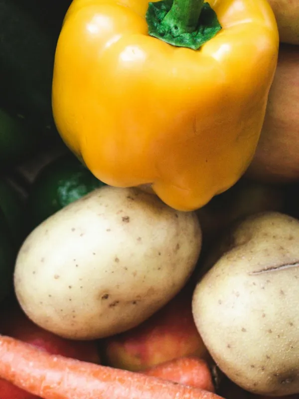 Close-up of a yellow bell pepper, two potatoes, and some carrots.