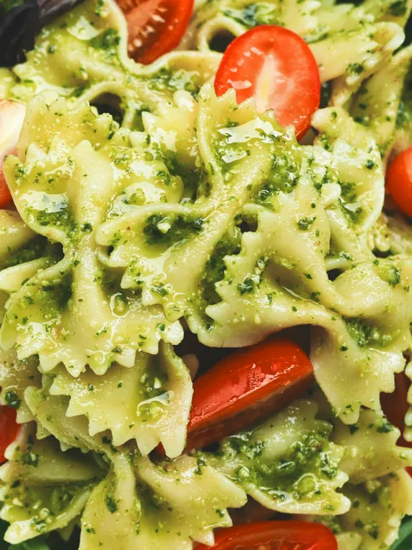 Close-up of bowtie pasta coated in green pesto sauce with cherry tomato halves.