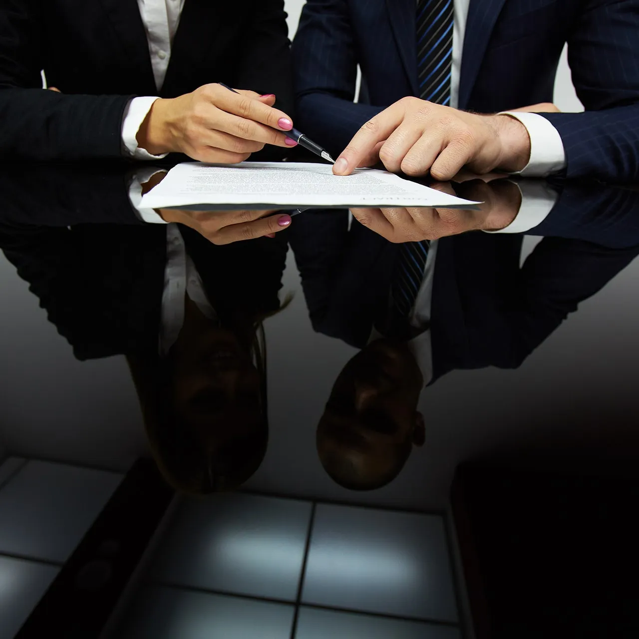 Two business professionals pointing and discussing a document on a reflective black table.