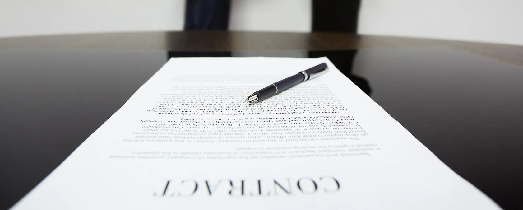 Contract document on a dark polished table with a black pen resting on top.