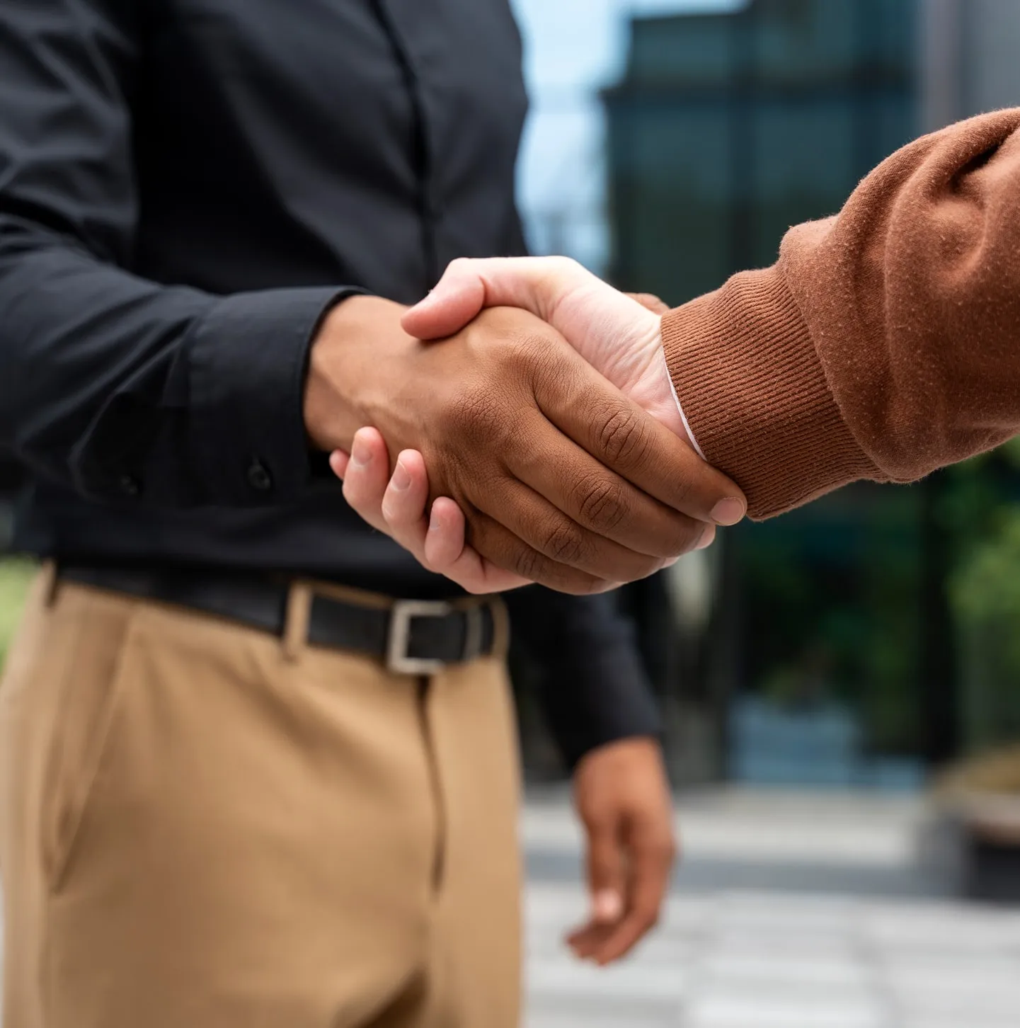 Two people in casual business attire shaking hands outside an office building.