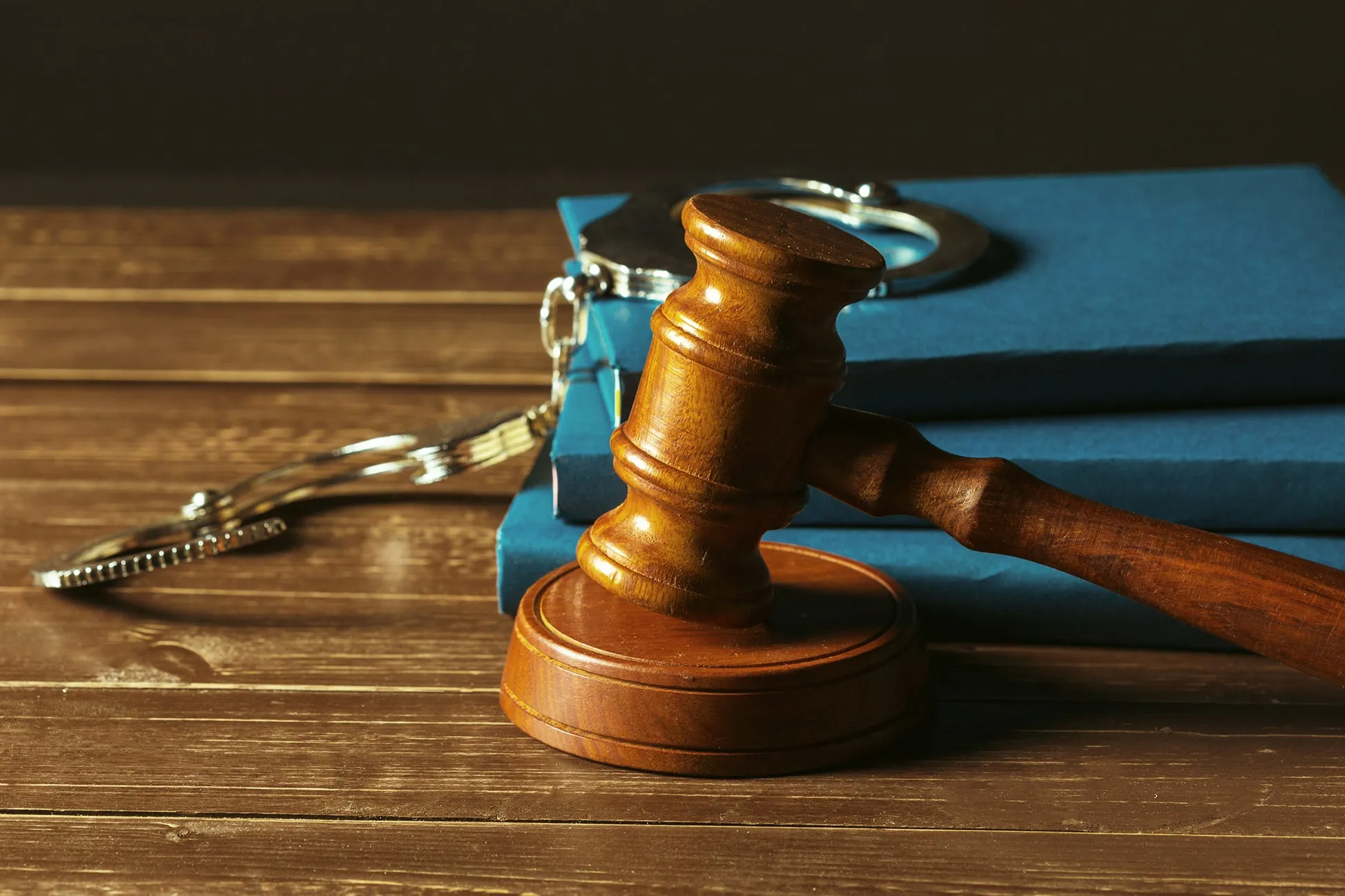 Wooden judge's gavel resting on a wooden surface with stacked blue books and silver handcuffs in the background.