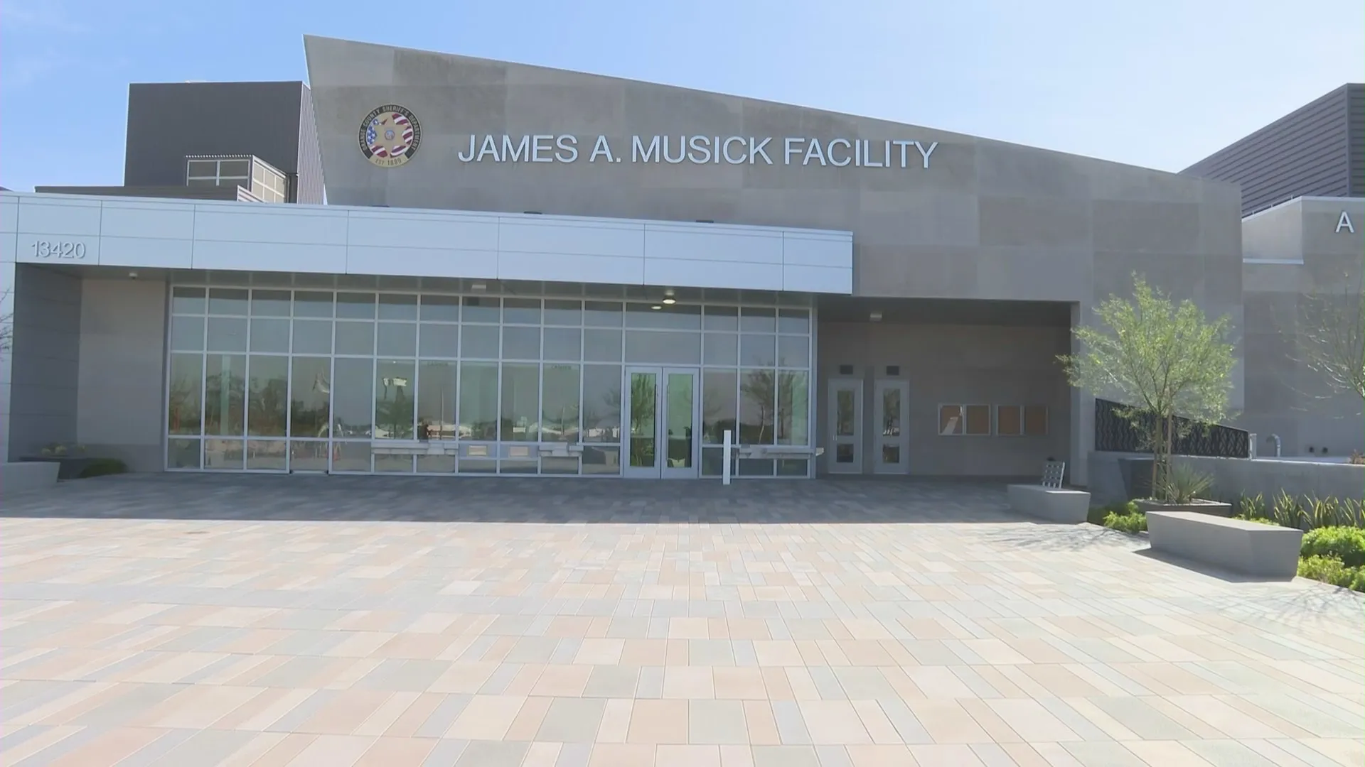 Exterior of James A. Musick Facility with large tiled courtyard and glass entrance doors under a clear sky.