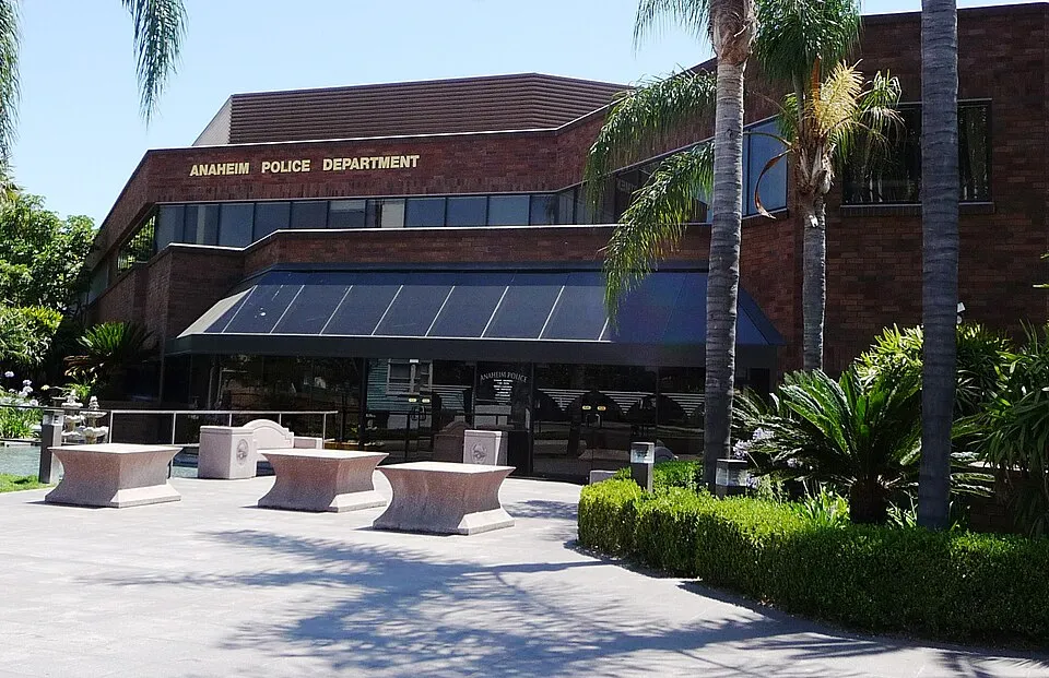 Exterior of the Anaheim Police Department building with brick facade, palm trees, and stone benches in front.