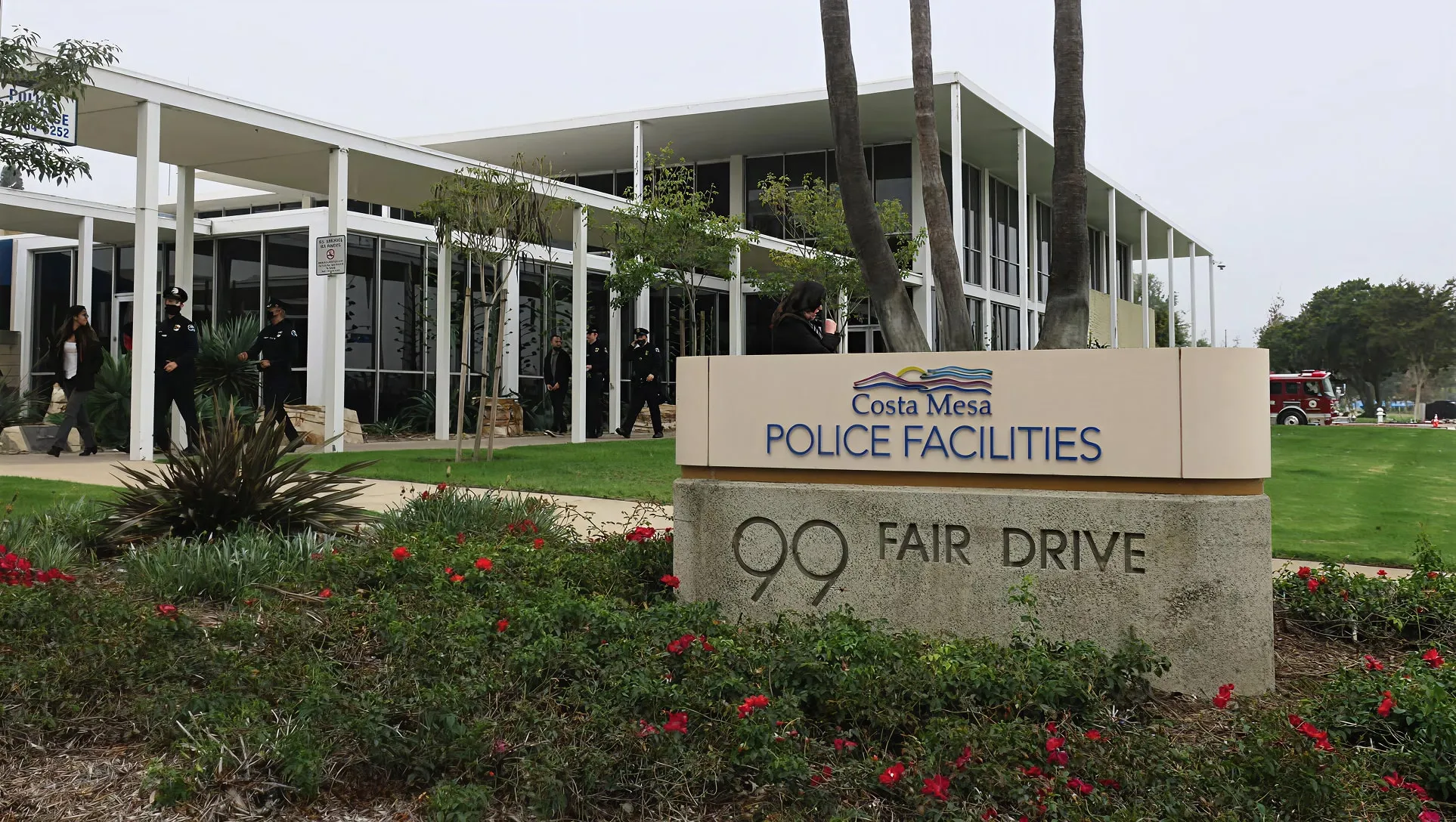Entrance to Costa Mesa Police Facilities at 99 Fair Drive with a modern building, green lawn, and red flowers in front.