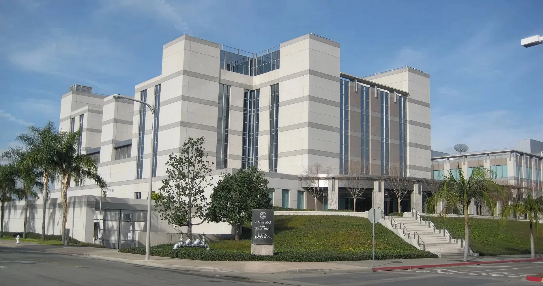 Modern multi-story building of Santa Ana Jail and Courthouse with palm trees and clear sky.