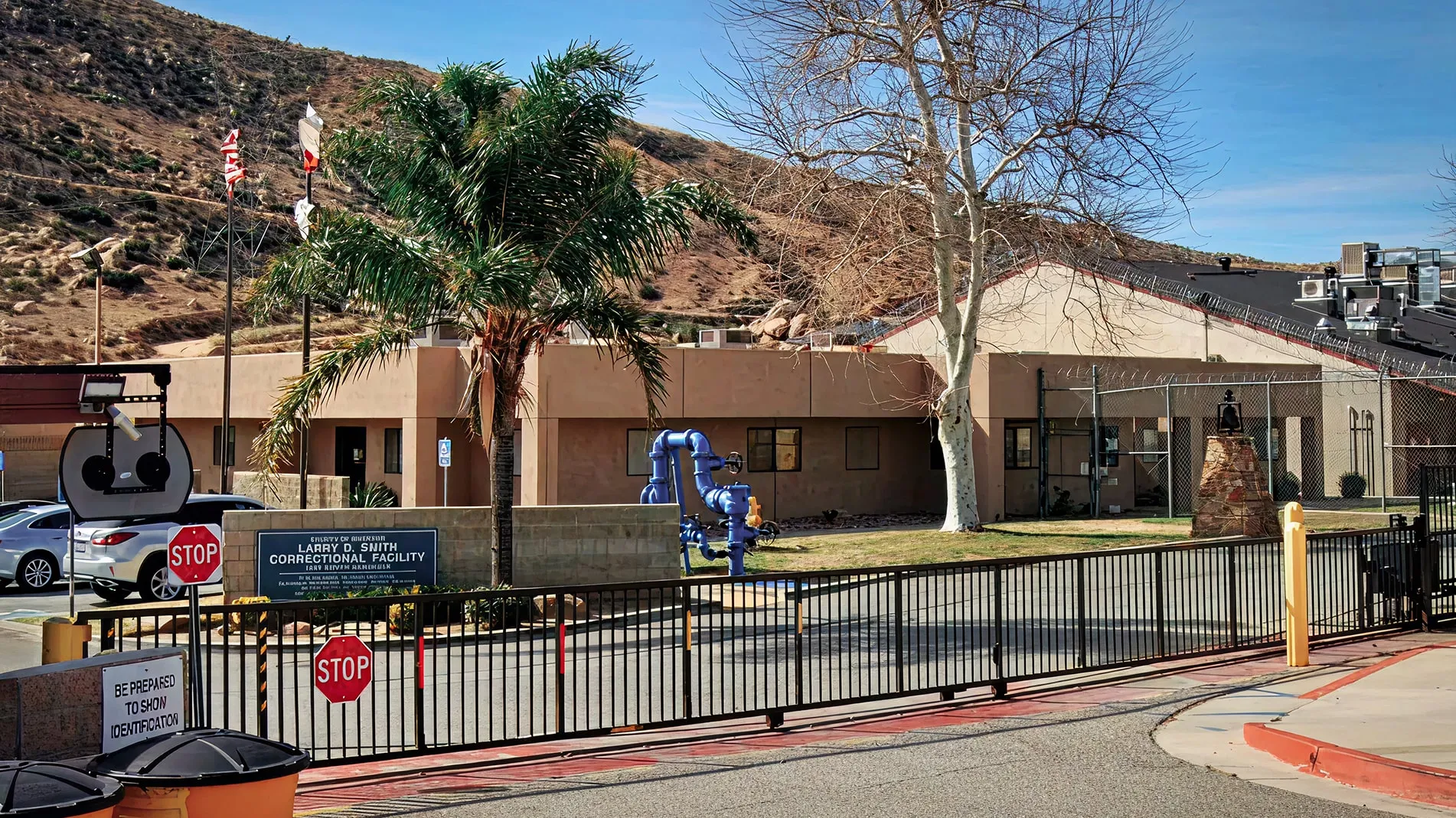 Entrance to Larry D. Smith Correctional Facility with stop signs, security gate, and a dry hillside in the background.