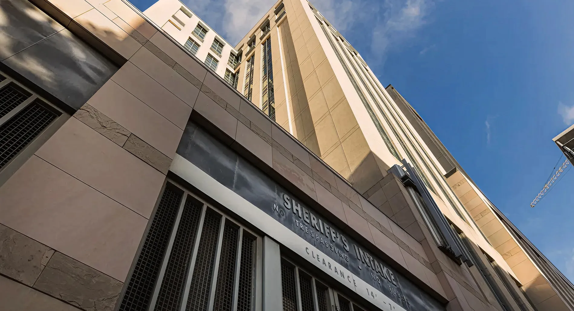 Low-angle view of a multi-story sheriff's intake building with barred windows and a blue sky background.