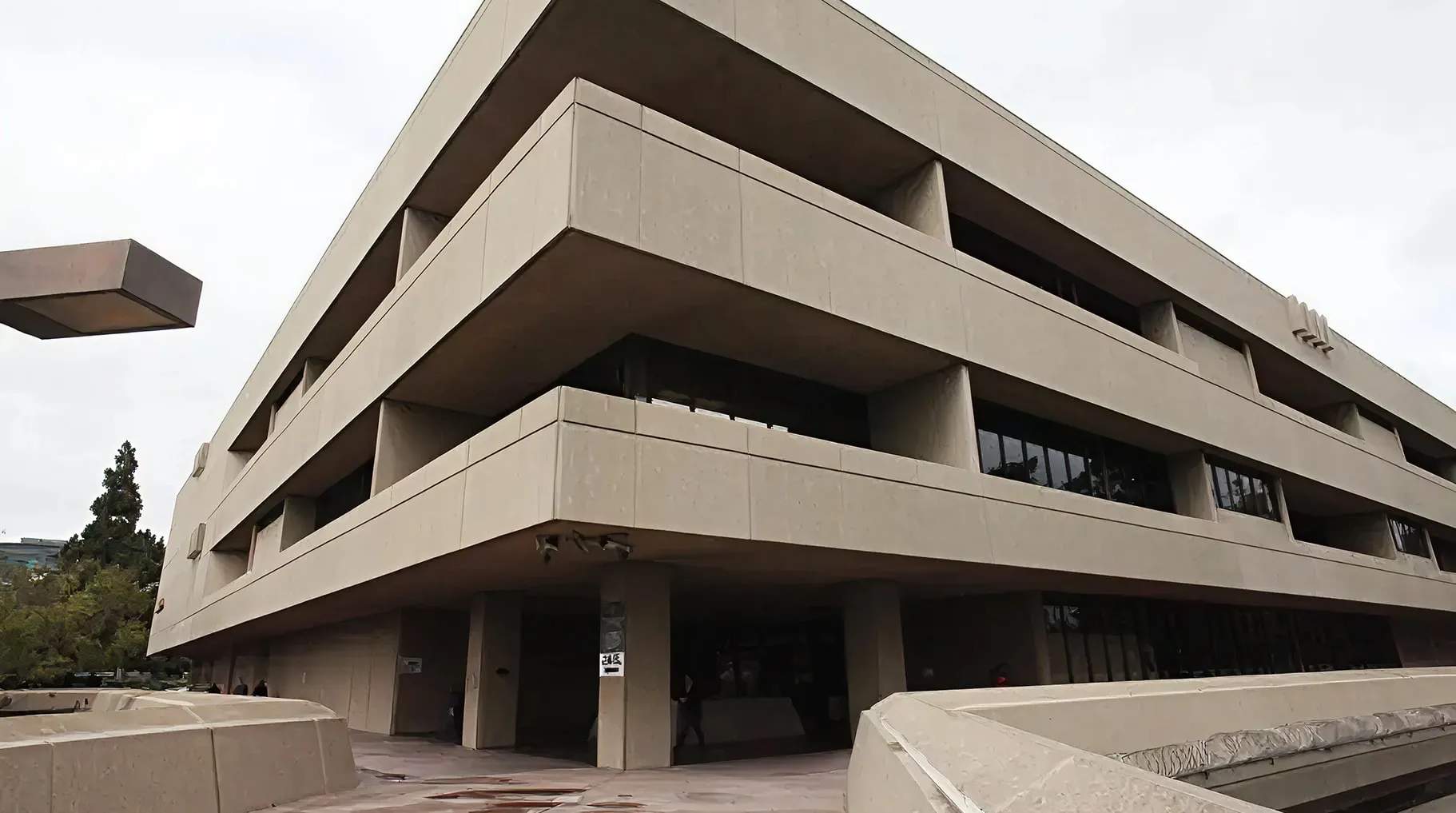 Exterior of a large, modern gray concrete building with angular balconies and horizontal windows.
