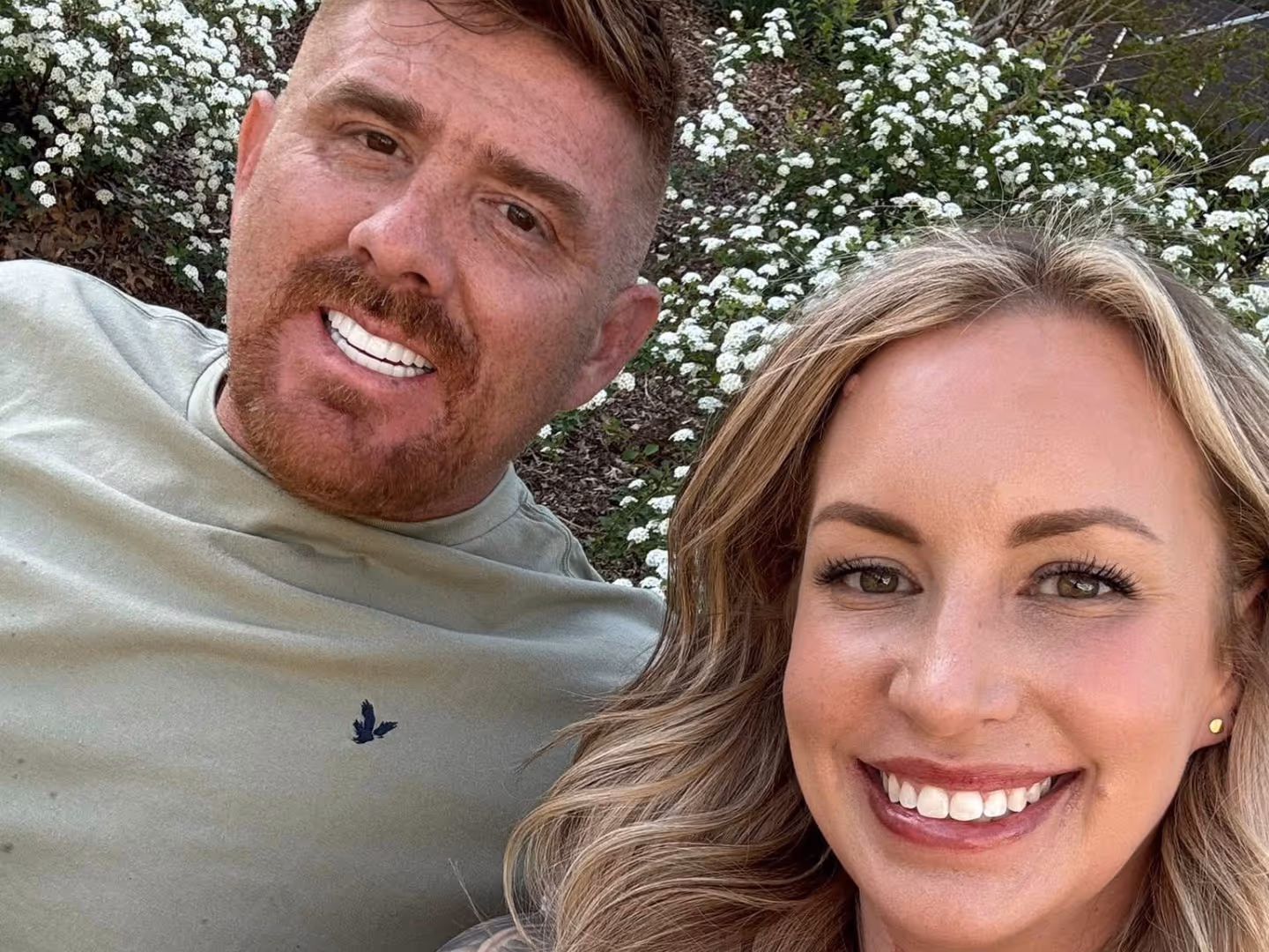 Close-up of Matthew Maloy and his wife Katelyn, both outdoors near white flowering bushes in Oklahoma City.
