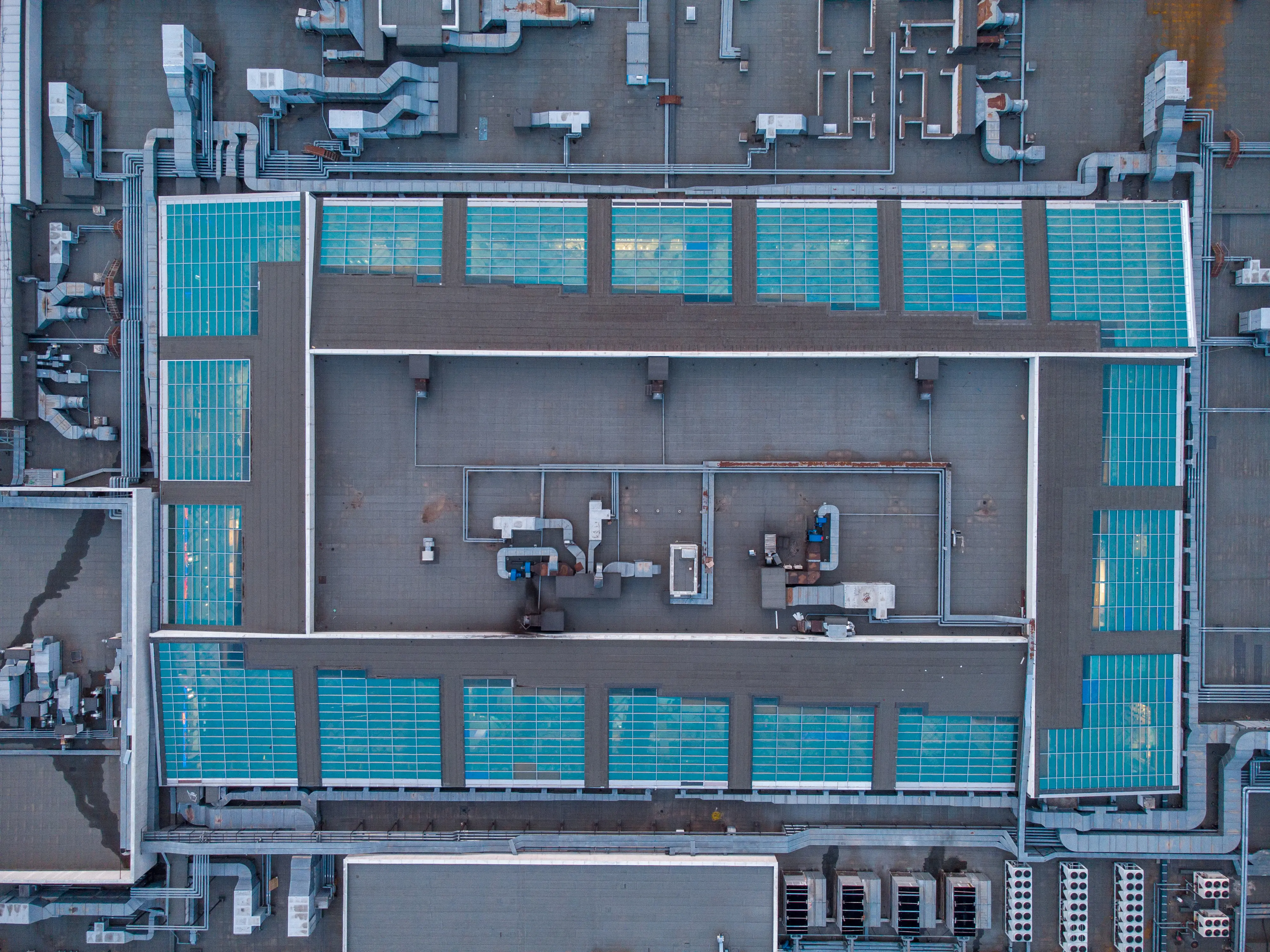 Aerial view of a large flat rooftop with multiple blue-tinted skylights and complex ventilation ducts.