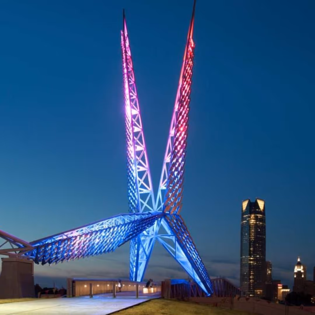 Illuminated Skydance Bridge in Oklahoma City at dusk with city skyscrapers in the background.