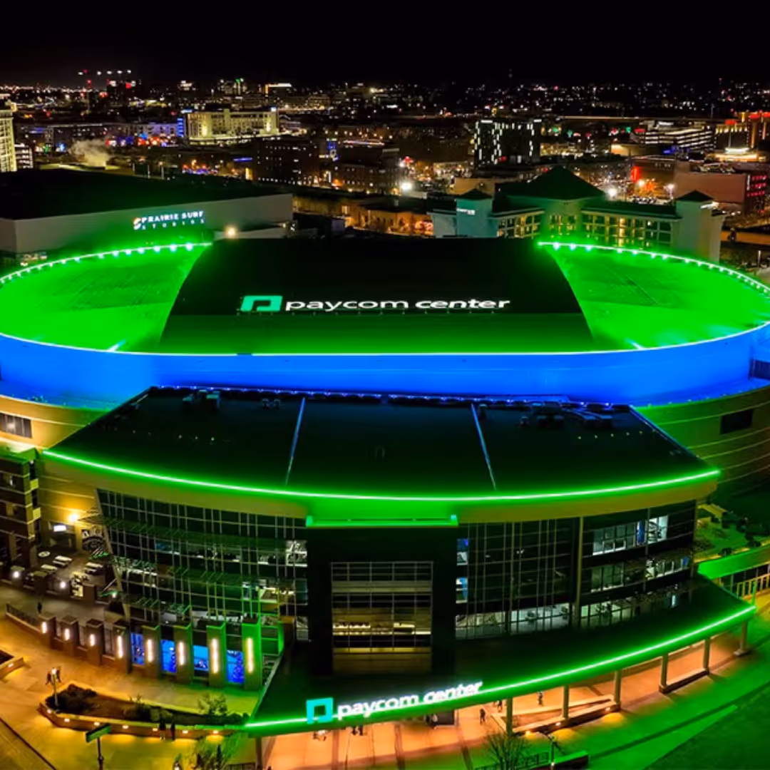 Aerial night view of Paycom Center in Oklahoma City illuminated with green and blue lights.