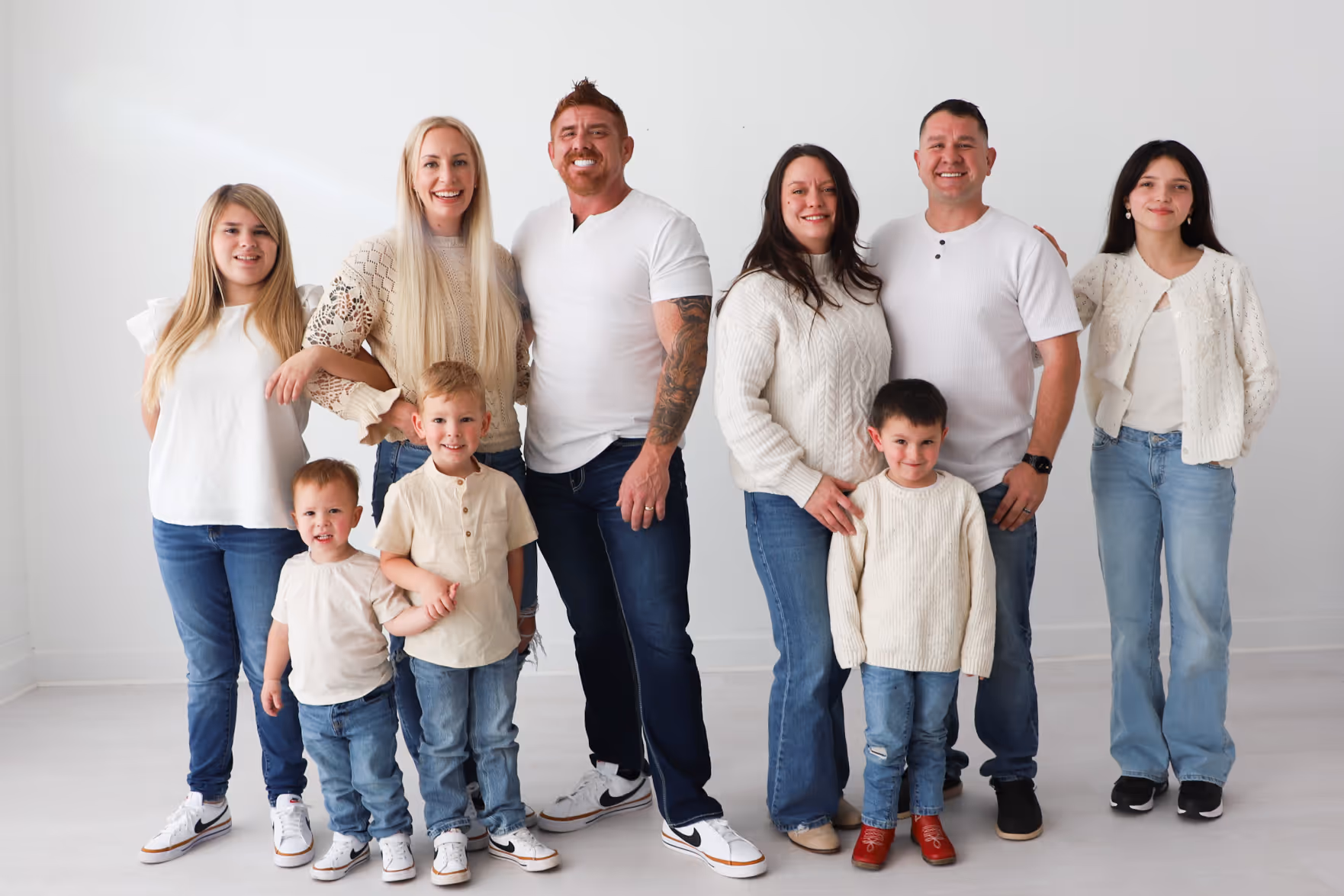 Group portrait of Roofing by Prodigy owners Matthew Maloy, Nicholas Mullaney and their families, standing together against a white background, all wearing casual white and light-colored tops with blue jeans.