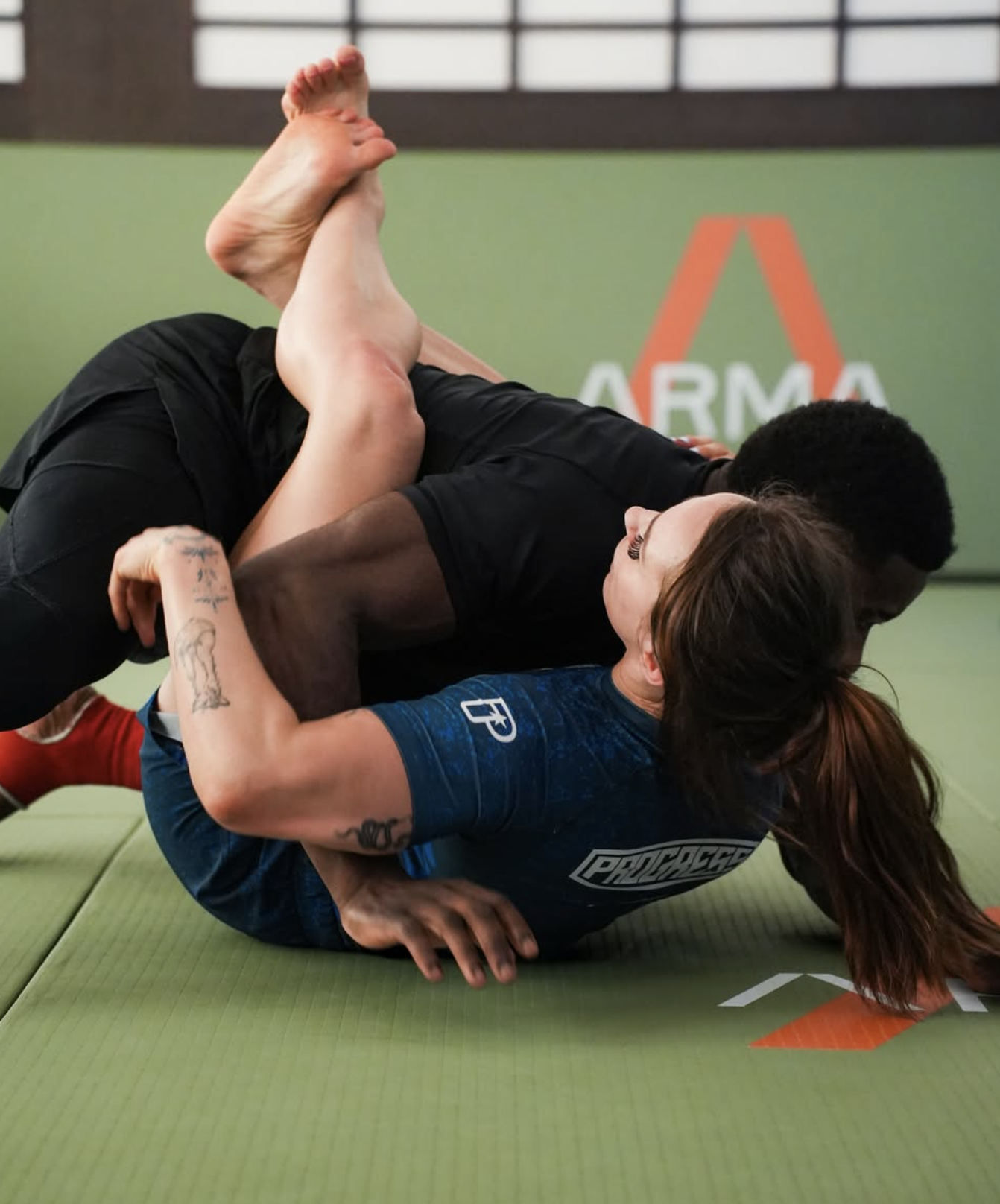Two BJJ practitioners grappling in no-gi training at ARMA Clapham, woman defending from bottom guard position