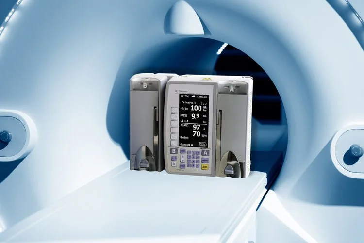 MRI machine with an infusion pump placed on the patient table inside the scanner opening.