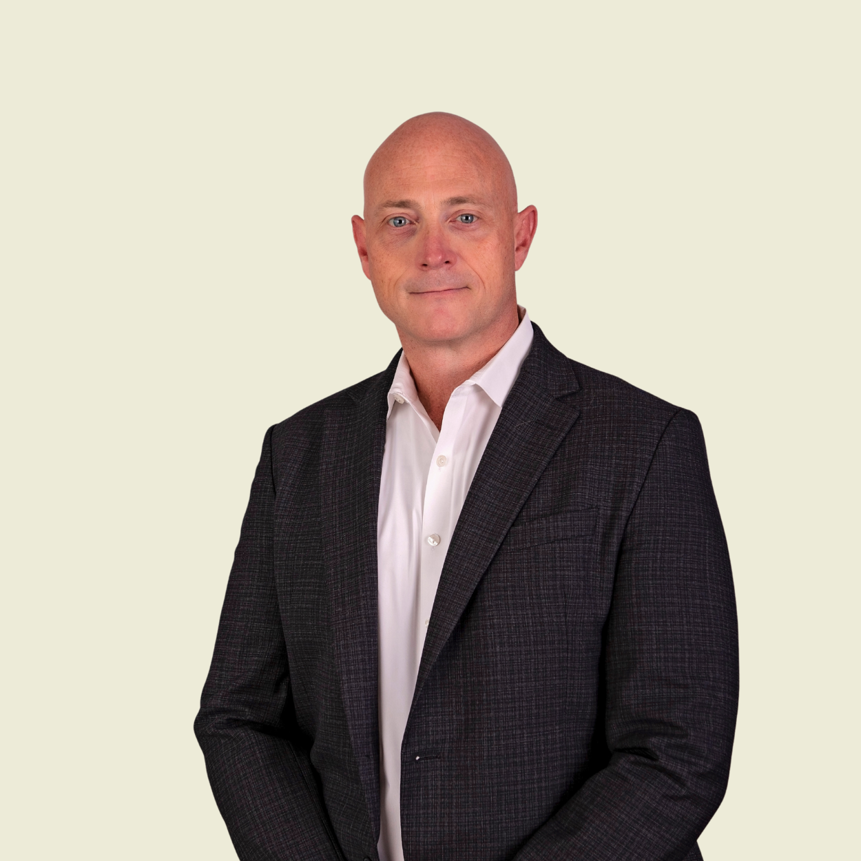 Bald man wearing a dark checkered blazer and white shirt against a light beige background.