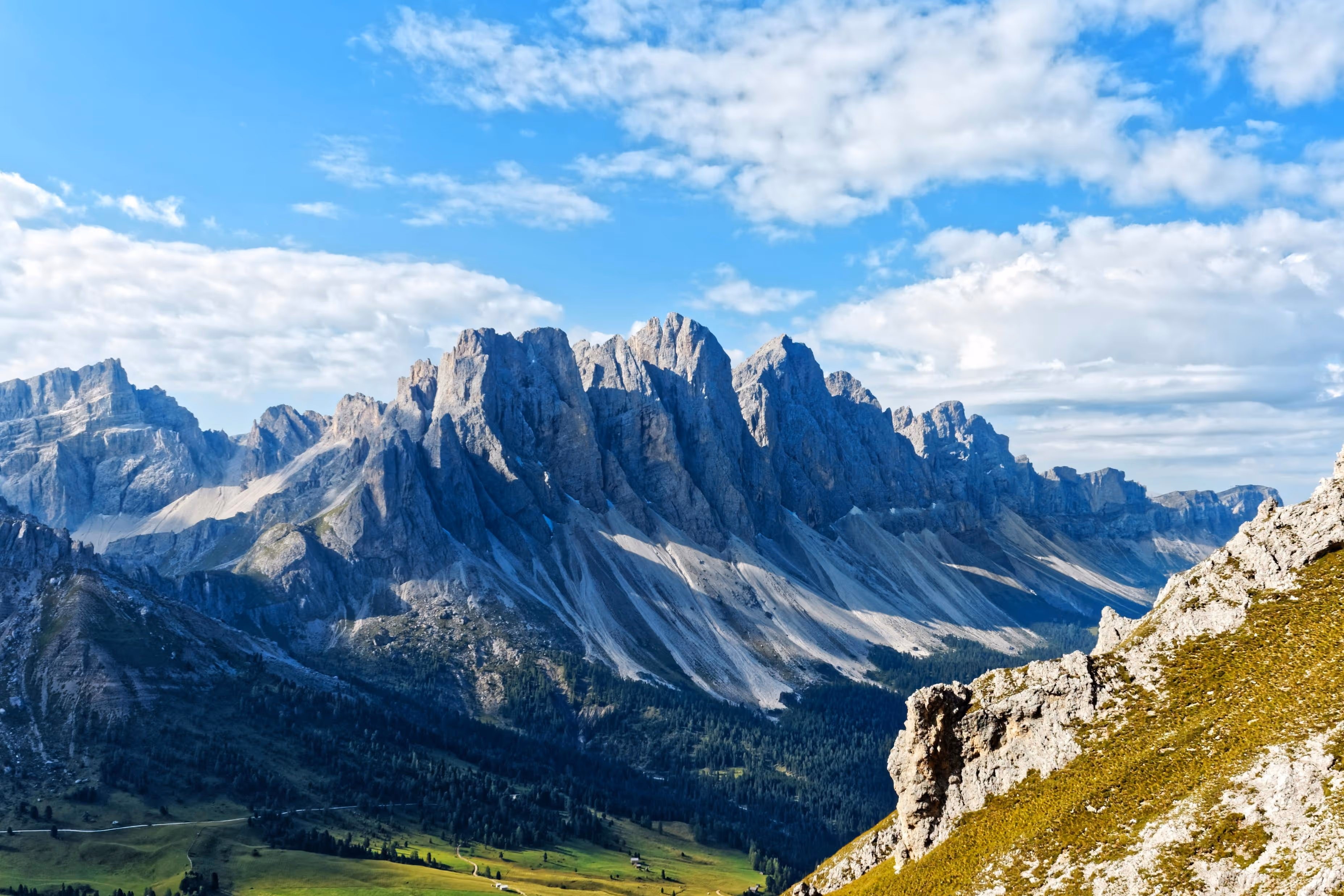 Blick auf eine felsige Bergkette mit grünen Tälern und blauem Himmel mit Wolken.