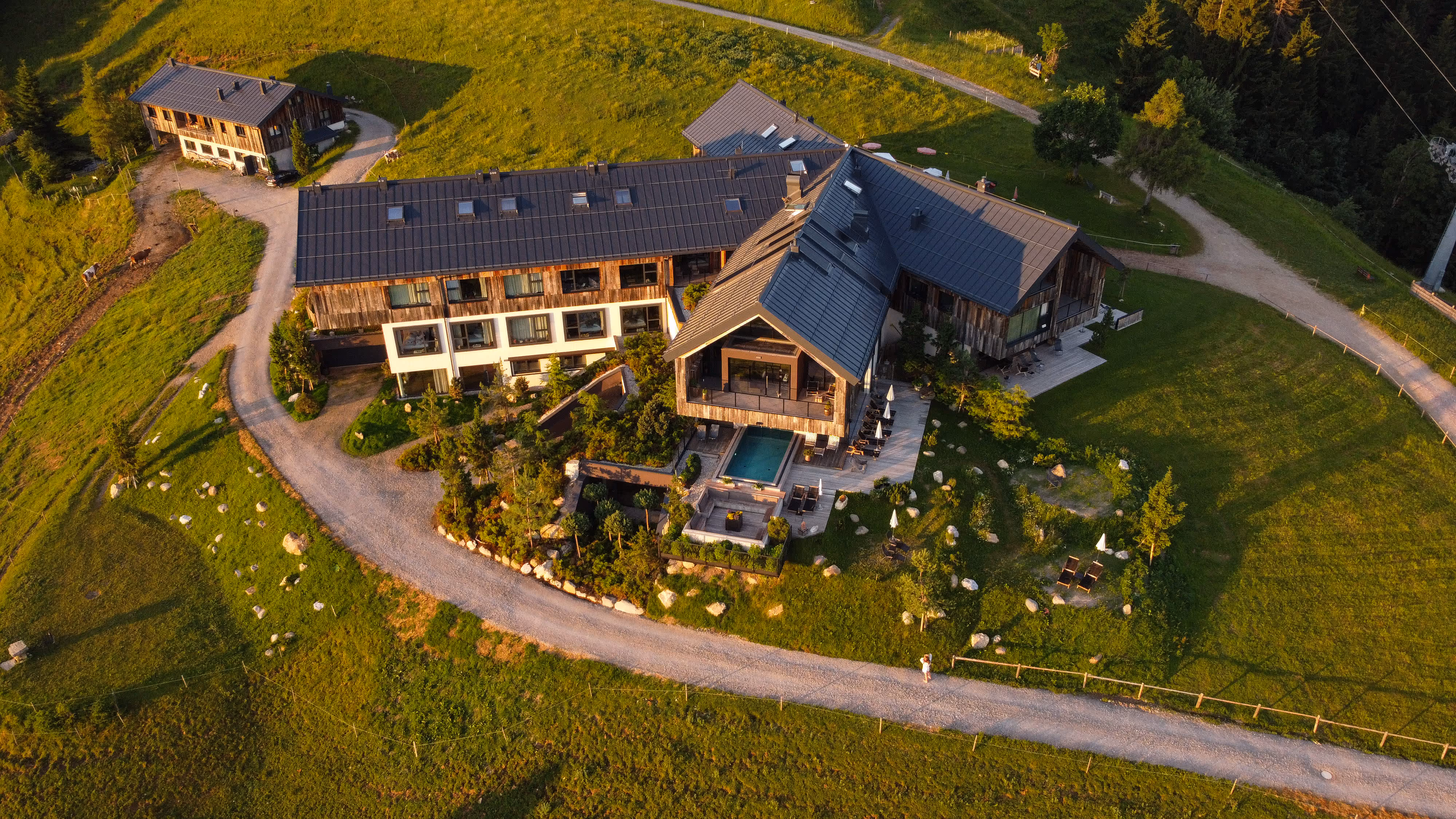 Luftaufnahme eines großen, modernen Landhauses mit angrenzendem Garten, Pool, gepflastertem Weg und umgeben von grünen Wiesen.