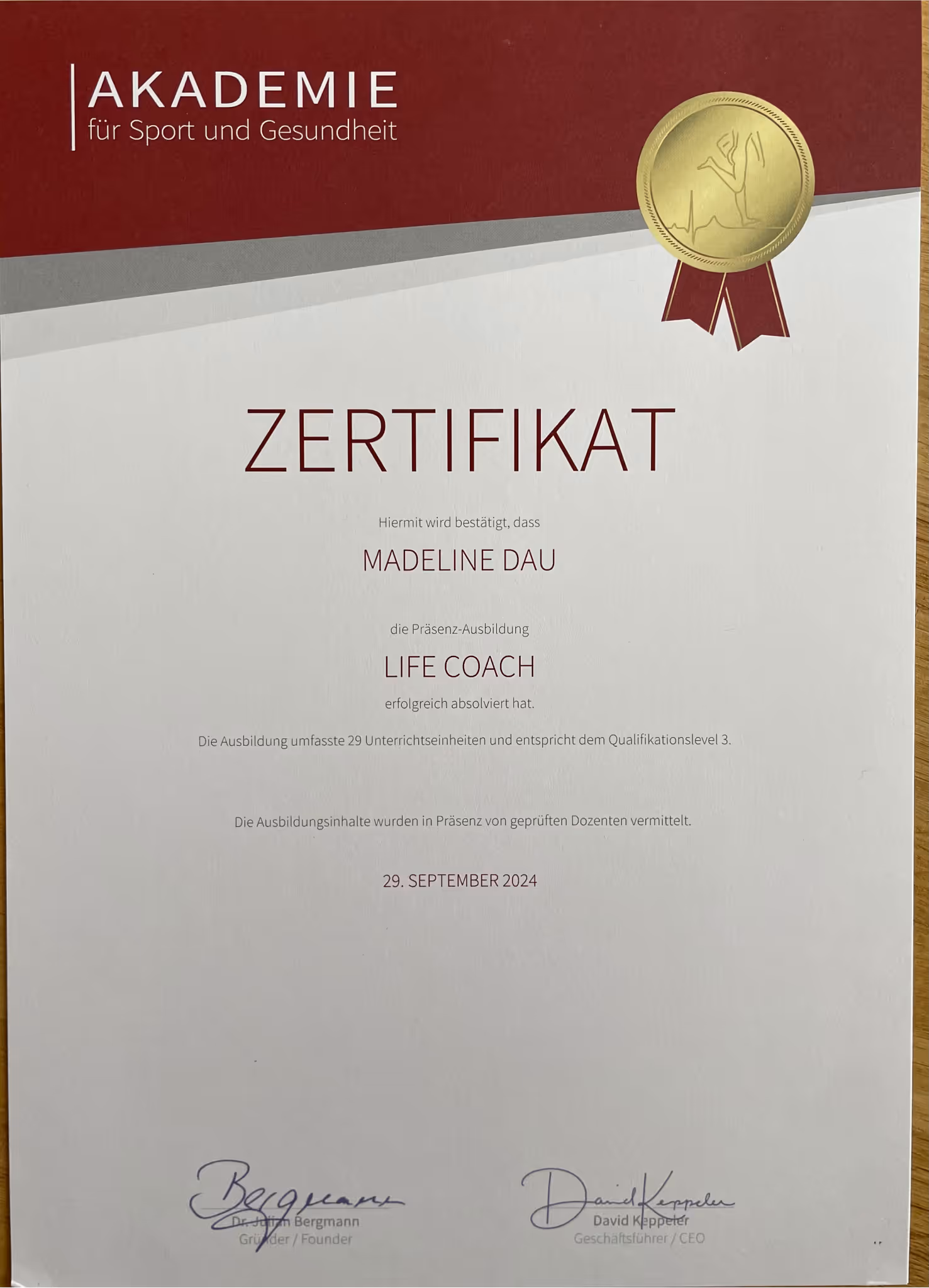 Zertifikat der Akademie für Sport und Gesundheit bestätigt, dass Madeline Dau die Life Coach Präsenz-Ausbildung erfolgreich abgeschlossen hat, datiert auf 29. September 2024, mit Unterschriften der Gründer und Geschäftsführer.