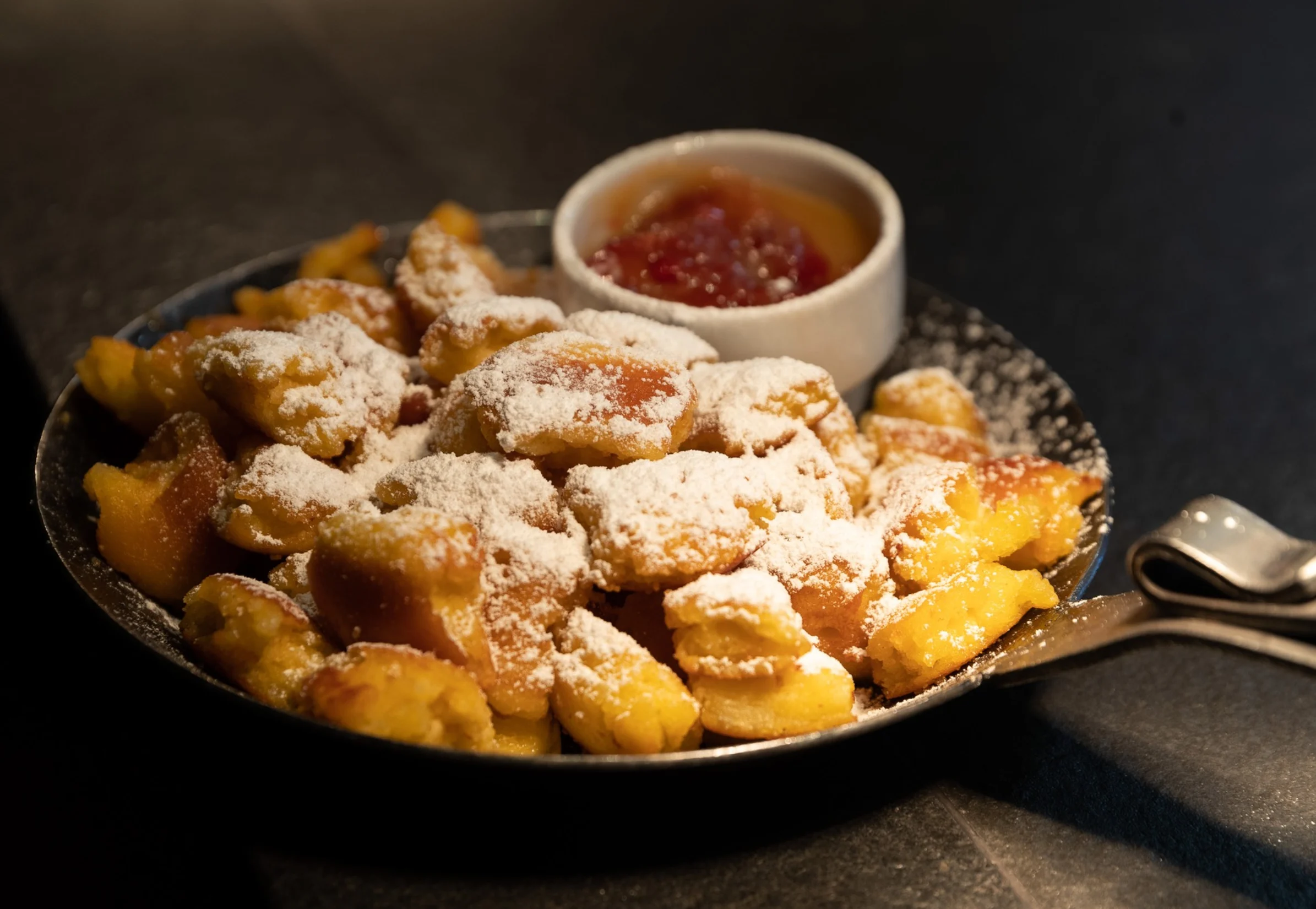 Portion Kaiserschmarrn mit Puderzucker bestreut und einer kleinen Schale Marmelade.