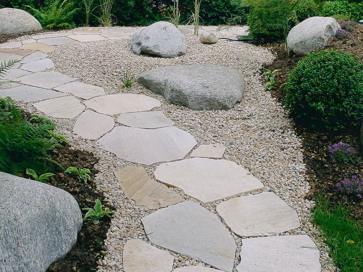 Naturstein Gartenweg mit hellen Trittplatten Kies in einer grünen gepflegten Gartenanlage