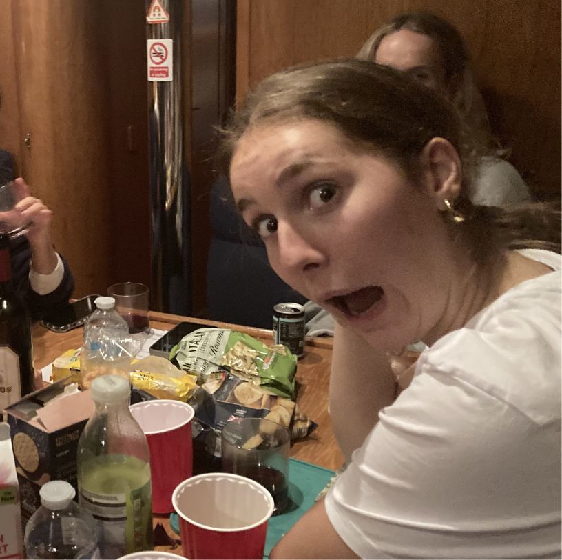 Young woman making a surprised or shocked face at a table with drinks and snacks.