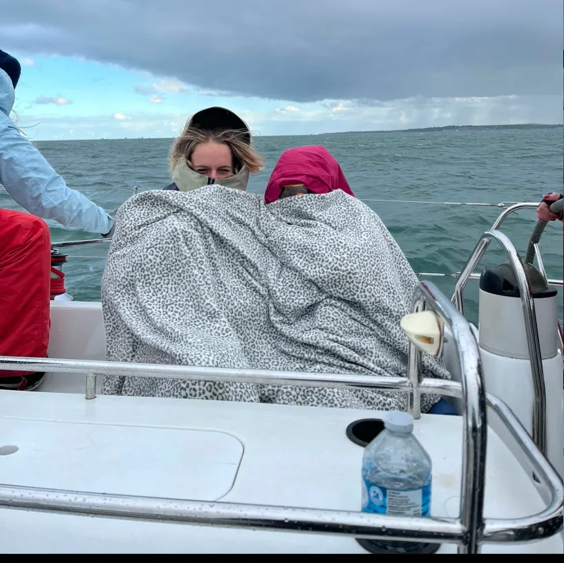 Two people wrapped in matching leopard-print blankets sitting close together on a boat with choppy ocean and cloudy sky in the background.