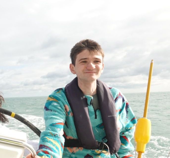 Smiling young man wearing a colorful fleece and life jacket steering a boat on a cloudy day.