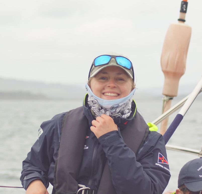 Smiling person wearing a life jacket, cap, and reflective sunglasses on a boat with water in the background.