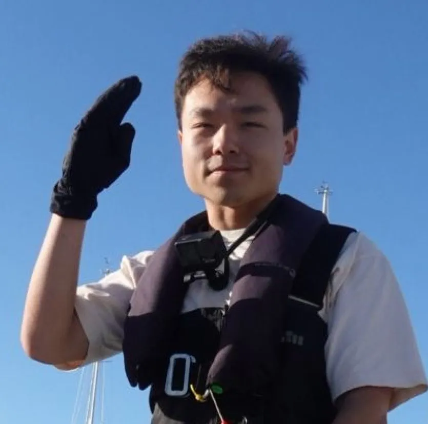 Man wearing black gloves and a life jacket saluting against a clear blue sky.