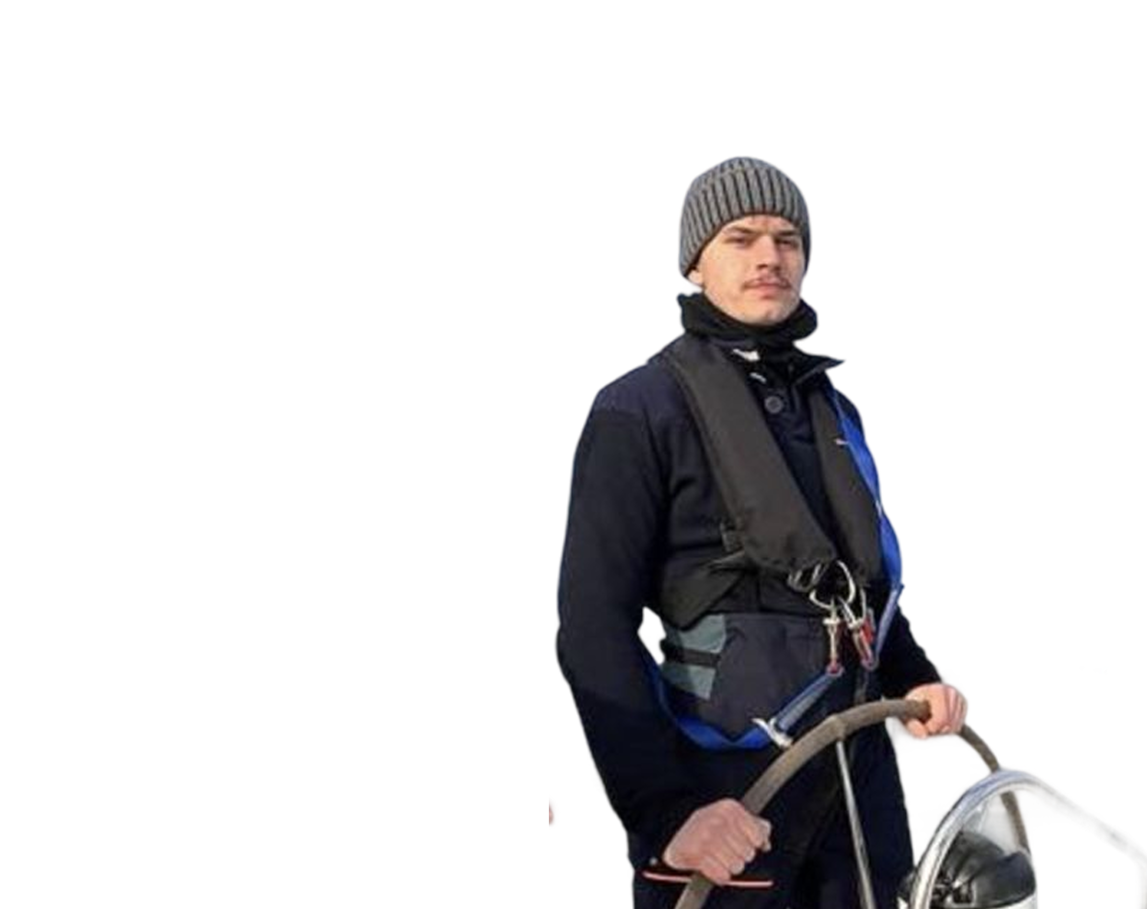 Man wearing a gray knit beanie, black jacket, and life vest steering a boat with a wooden wheel.