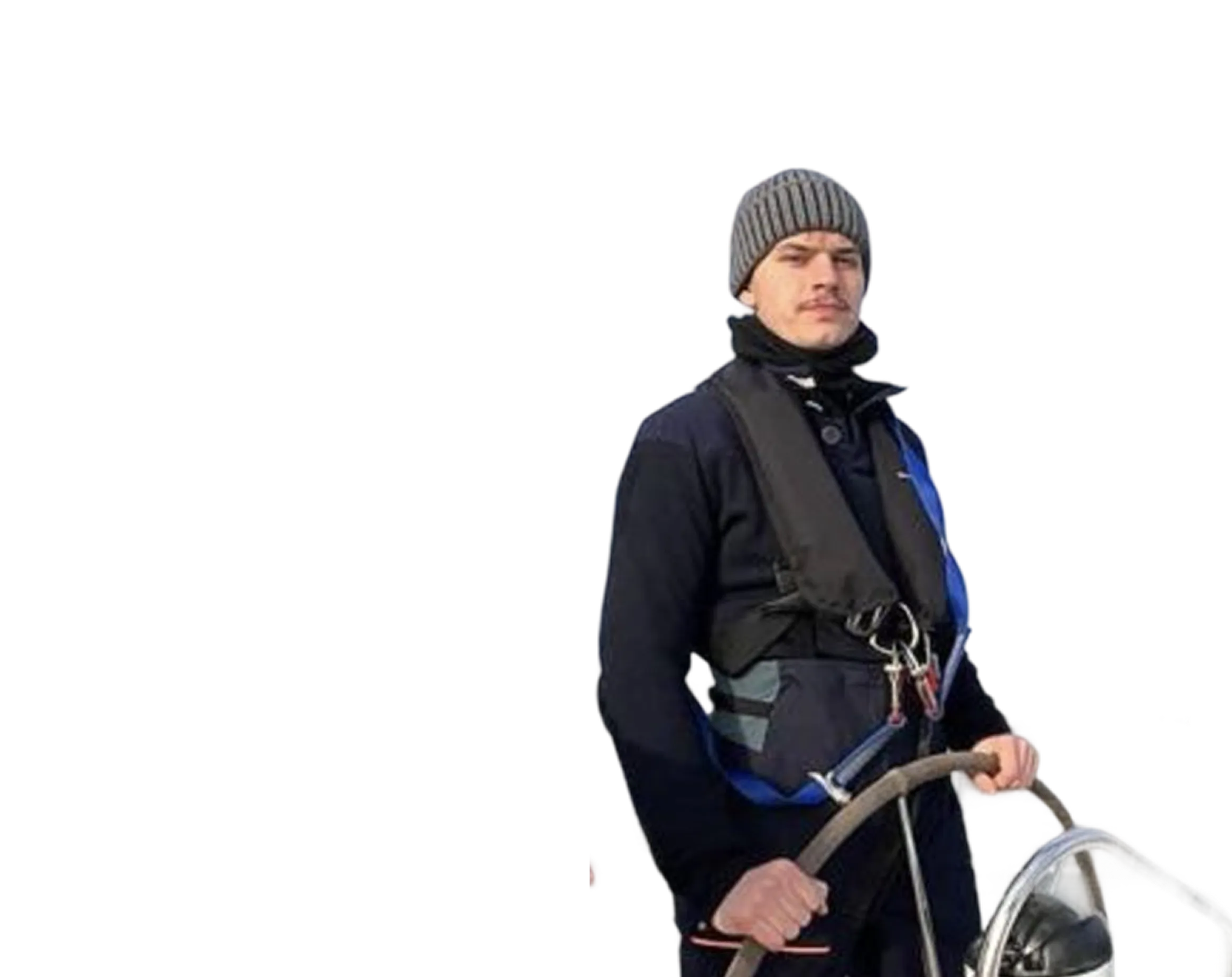 Man wearing a gray knit beanie, black jacket, and life vest steering a boat with a wooden wheel.