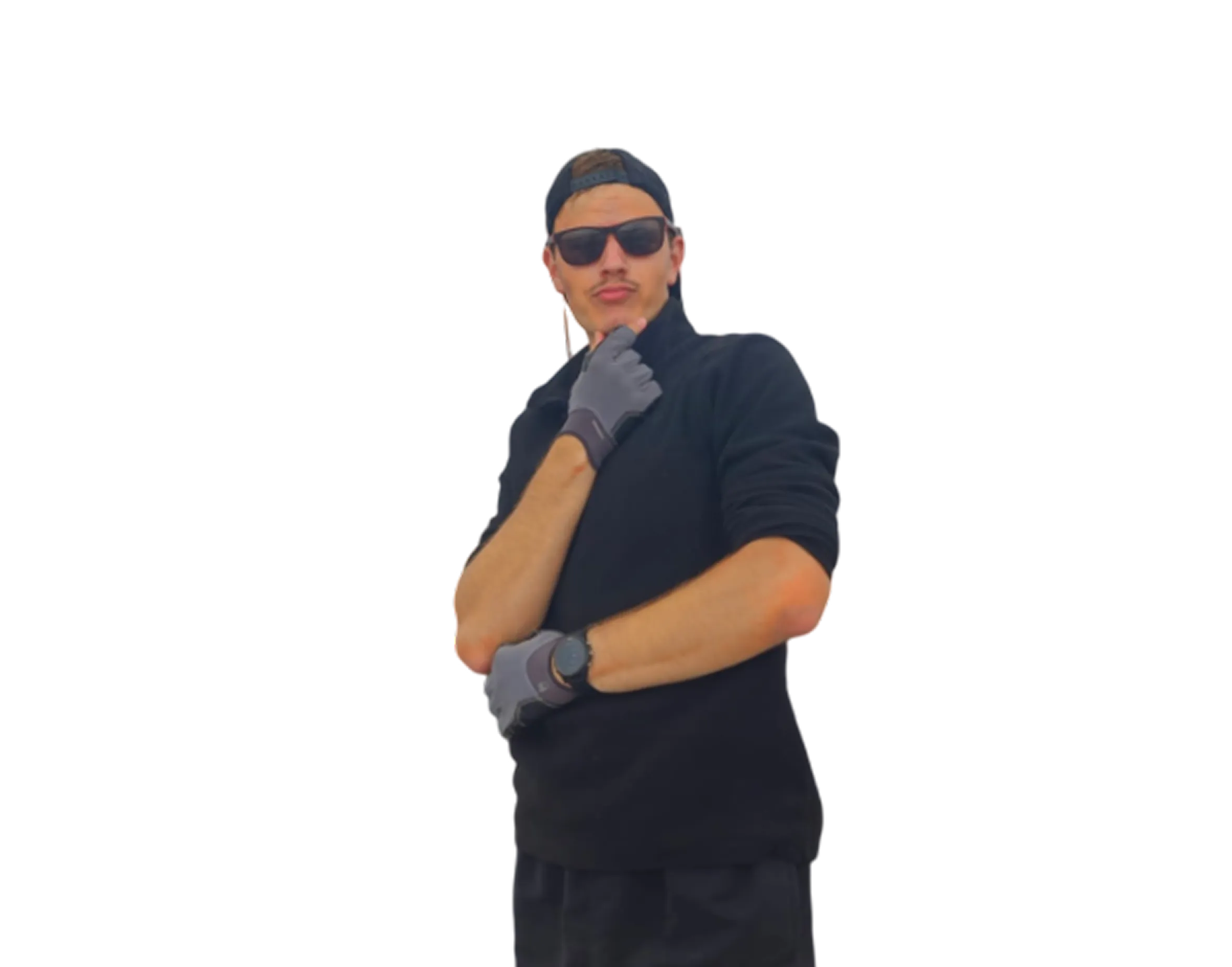 Man wearing black sunglasses, black cap backwards, black long-sleeve top, and gray gloves posing with one hand on chin and the other crossed.