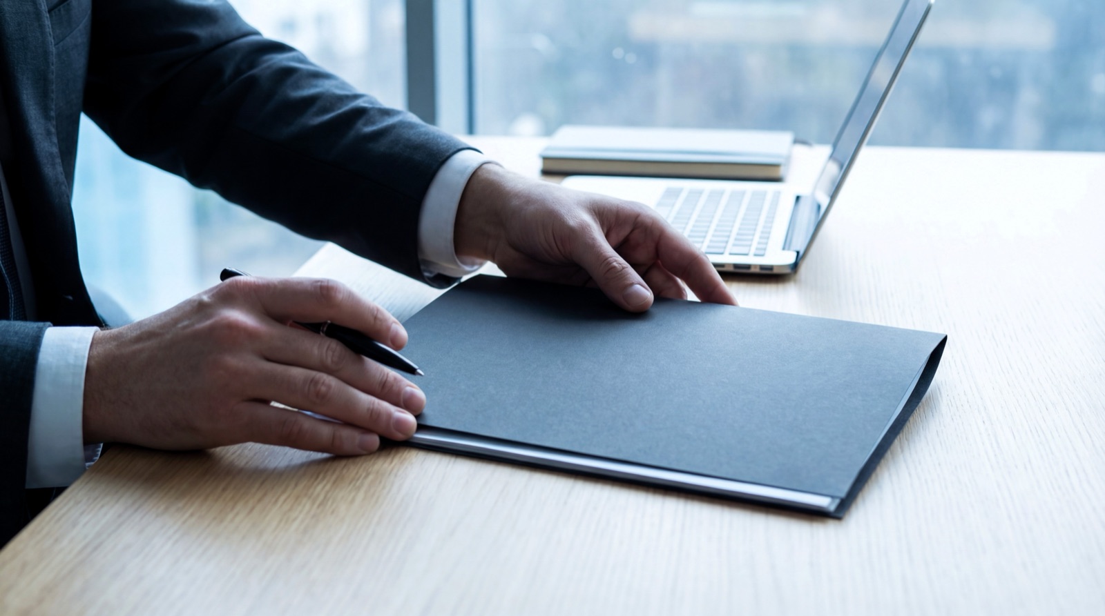 Mains posées sur un dossier fermé, à côté d'un ordinateur portable, sur un bureau