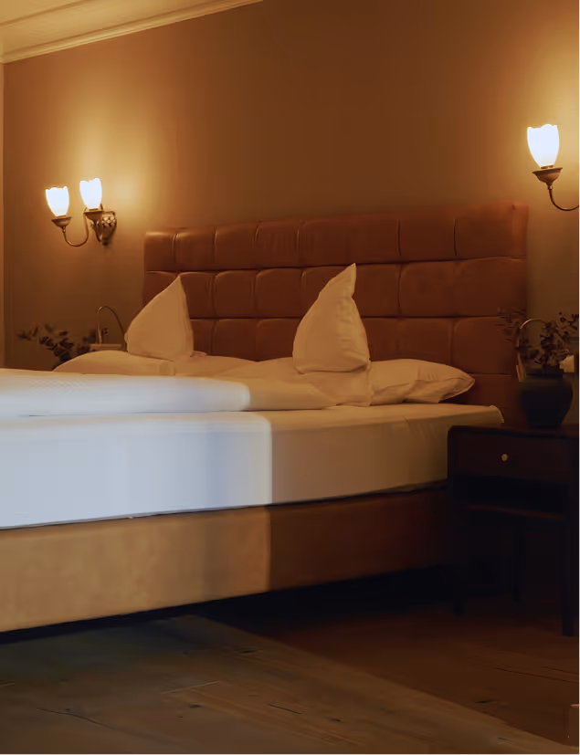 Elegantes Schlafzimmer der Suite Silberdistel mit warmem Licht, Lederkopfteil und Holzakzenten im Hotel Hohenfels.