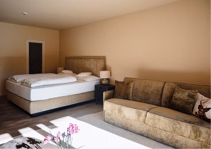 Suite Vilsalpsee mit Boxspringbett, samtbezogenem Sofa und warmem Licht – Komfort mit alpinem Charme.