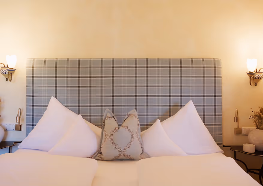 Doppelzimmer Edelweiß mit stilvollem, kariertem Kopfteil und warmem Licht – behagliche Atmosphäre im alpinen Stil.