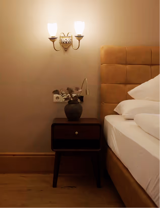 Elegantes Schlafzimmer der Suite Silberdistel mit warmem Licht, Lederkopfteil und Holzakzenten im Hotel Hohenfels.