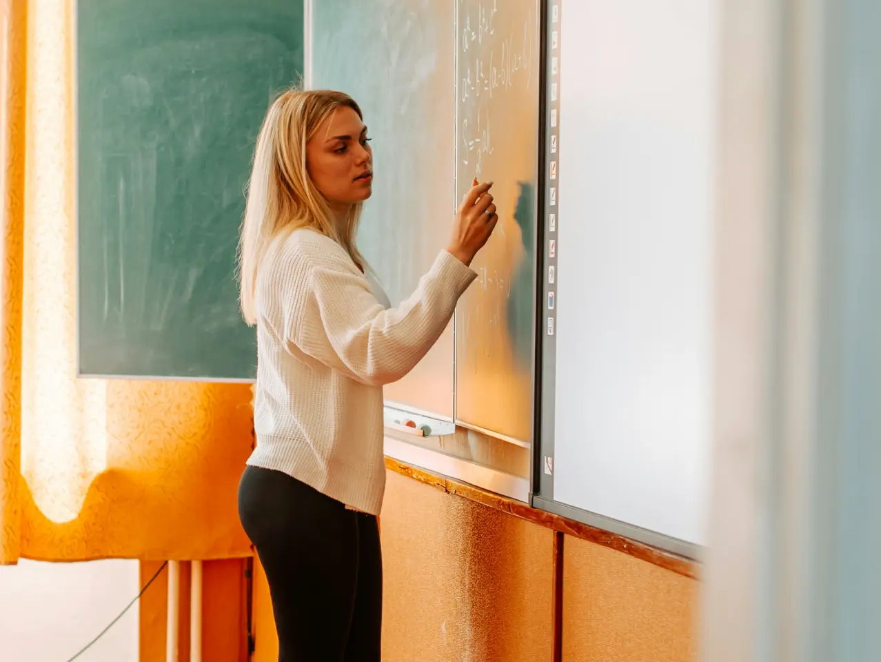 A woman writing mathematical equations on a chalkboard in a classroom.
