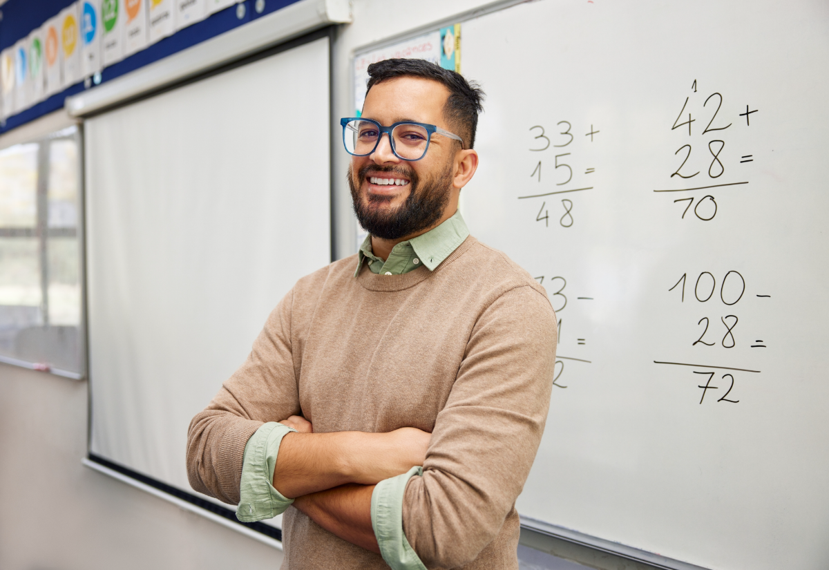 A smiling elementary math teacher standing at the whiteboard in his classroom