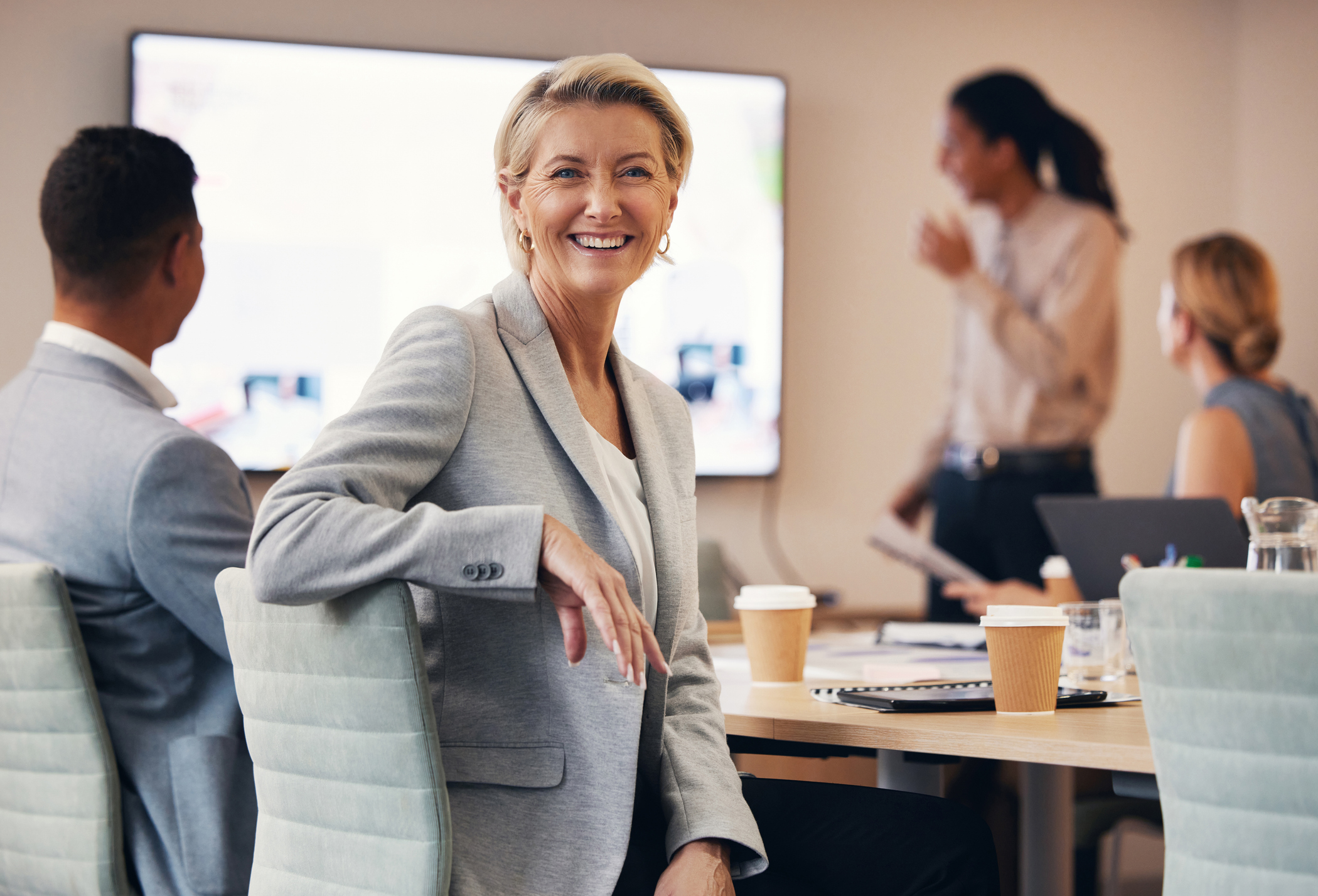 A smiling school district superintendent in a leadership meeting room with colleagues and a presentation screen